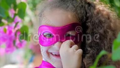 美丽的小女孩穿着超级英雄的服装，穿着粉红色的斗篷和英雄的面具。 坐在飞机上